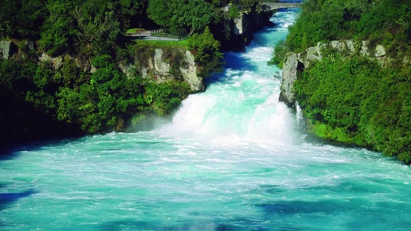 Blue water of the Huka Falls at Lake Taupo between green river banks