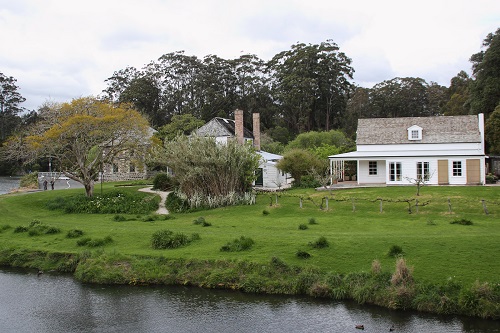 Two old buildings beside a river surrounded by gardens