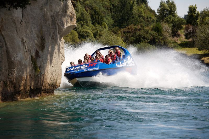 Passengers on a motorboat in the water beside a cliff at Huka Falls at Lake Taupo