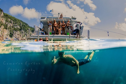 Diver under water with people on a boat above water in the background